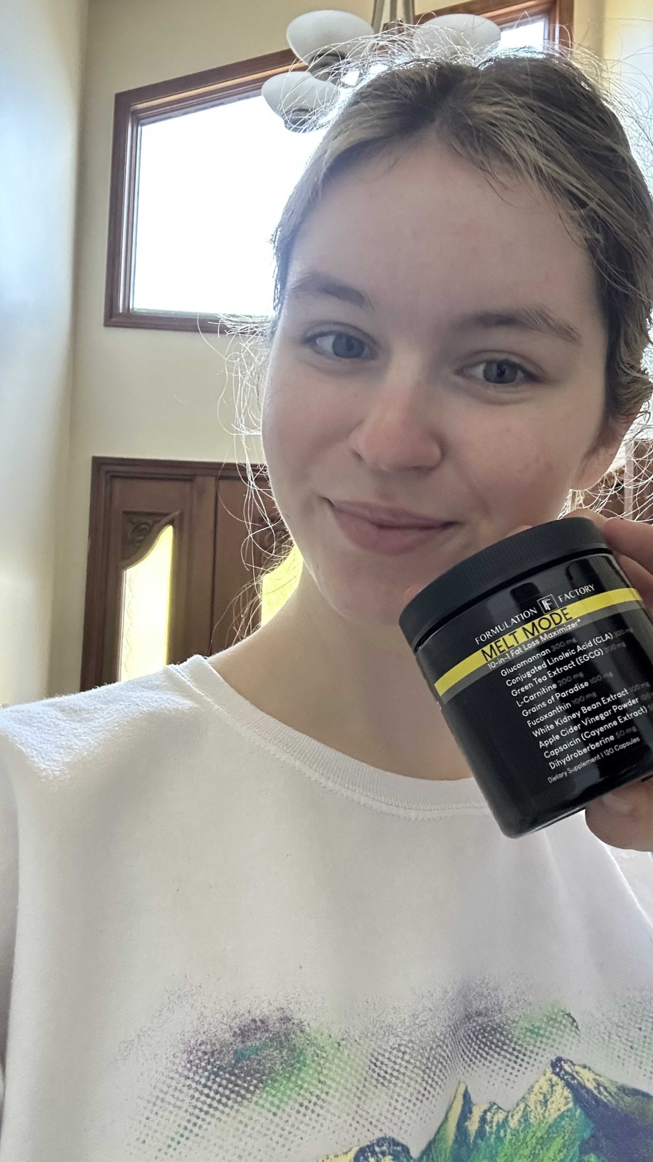 Person holding a black container with yellow label, smiling indoors.
