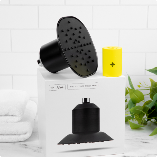 Shower head and yellow filter on a box, with towels and a plant nearby.
