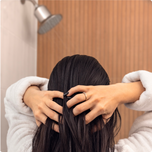 Person shampooing hair under showerhead.