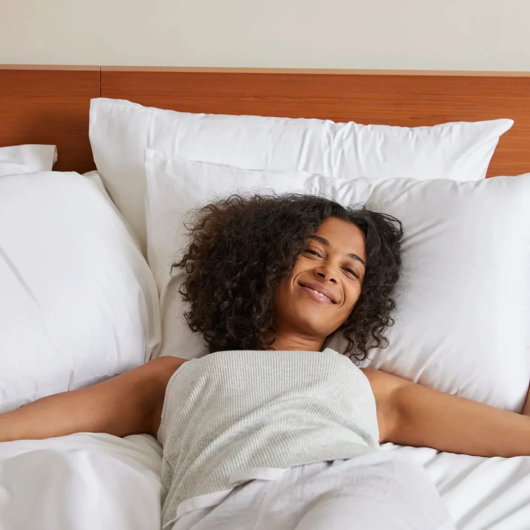 Person smiling while lying on a bed with white pillows.