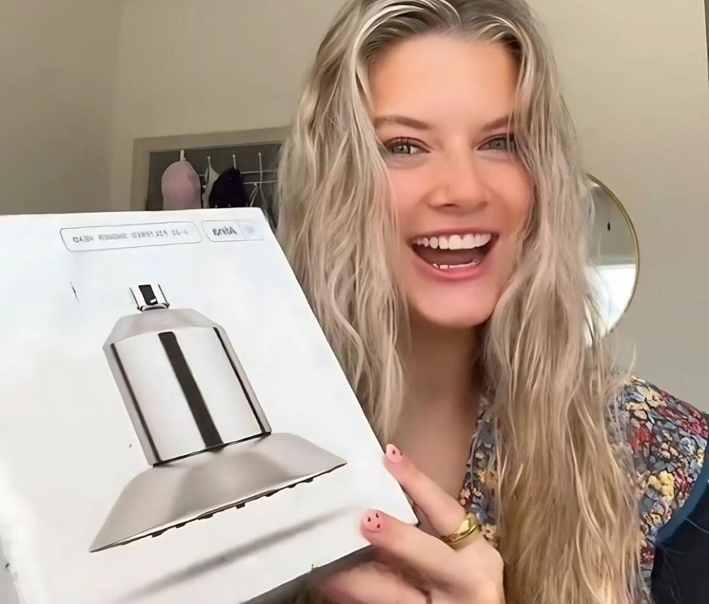 Person smiling and holding a box with a metallic shower head displayed.