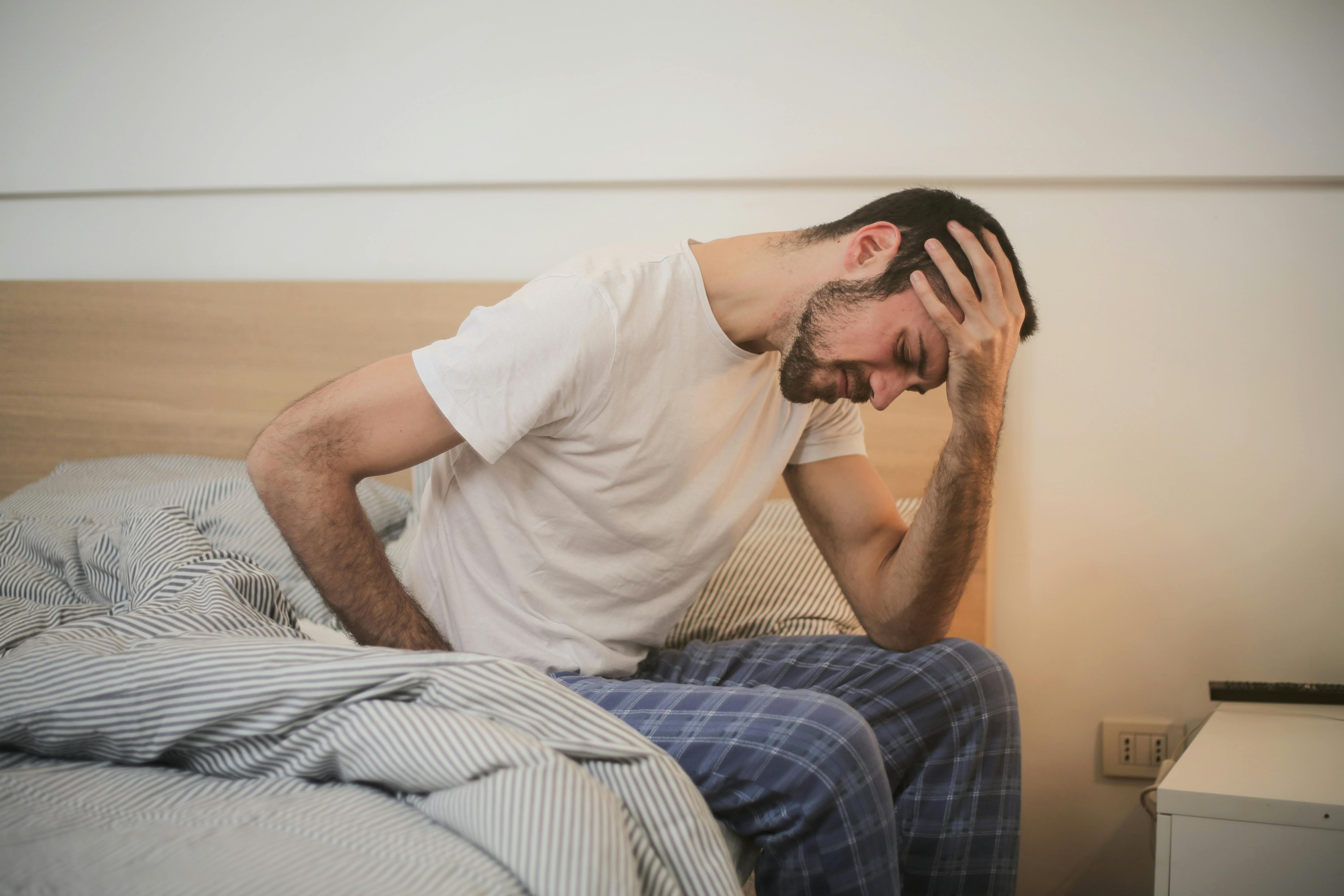 Man sitting on bed holding his head, appearing distressed.