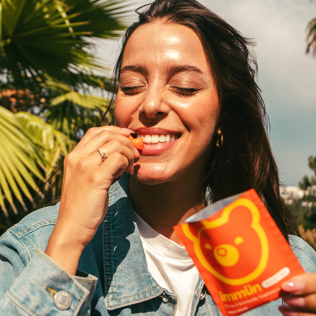 Woman smiling, holding a gummy bear near her mouth outdoors.