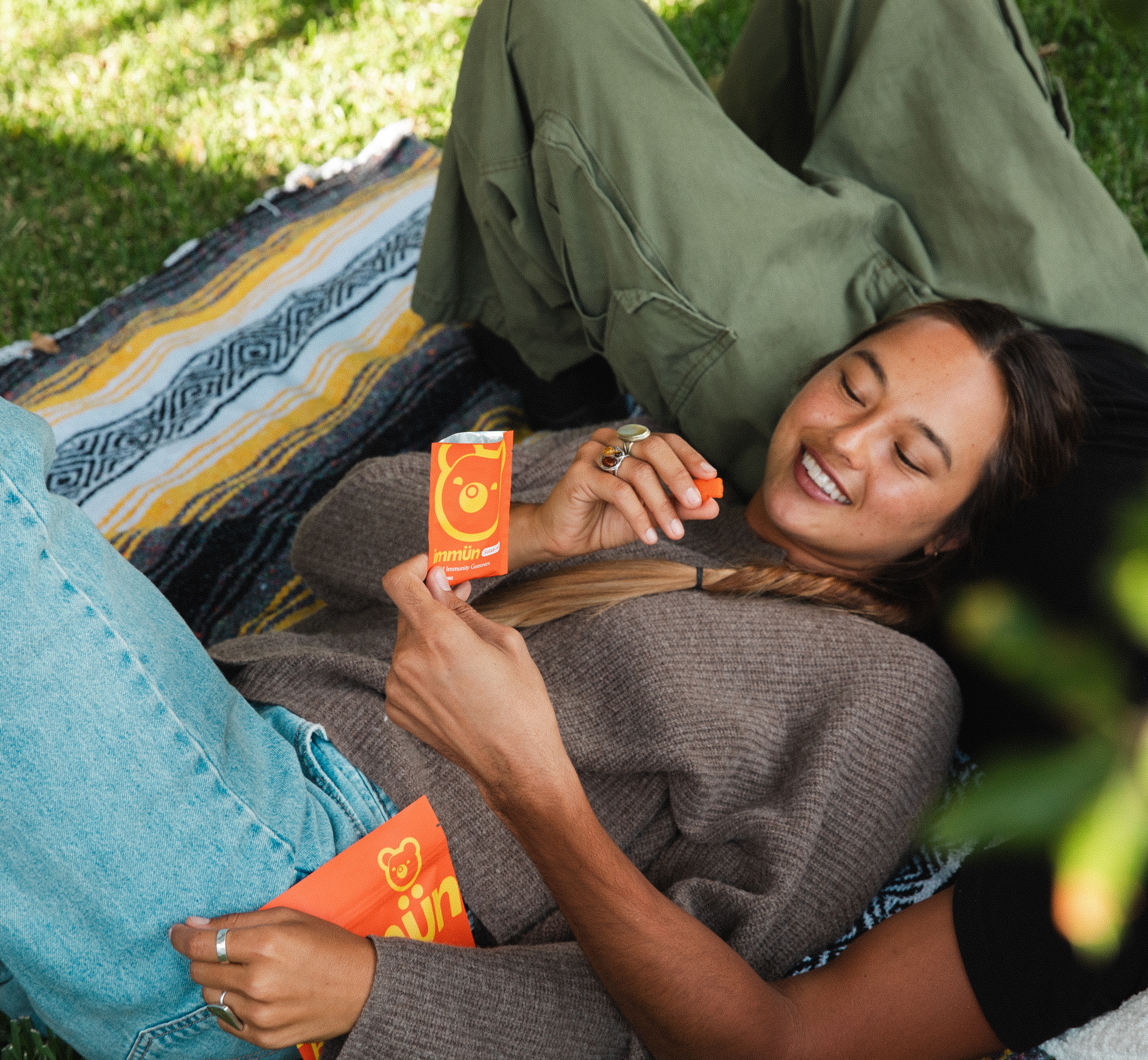 Person lying on blanket outdoors, holding a packet with an orange bear design.