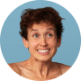 A headshot of a smiling woman with short, curly brown hair against a light blue circular background.