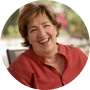 A circular headshot of a smiling woman with short brown hair wearing a red shirt.