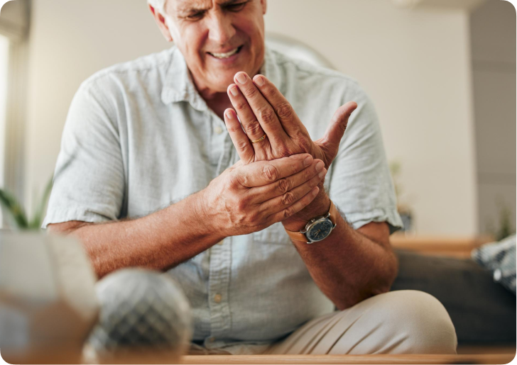 An older man with a pained expression sits while holding his hand.