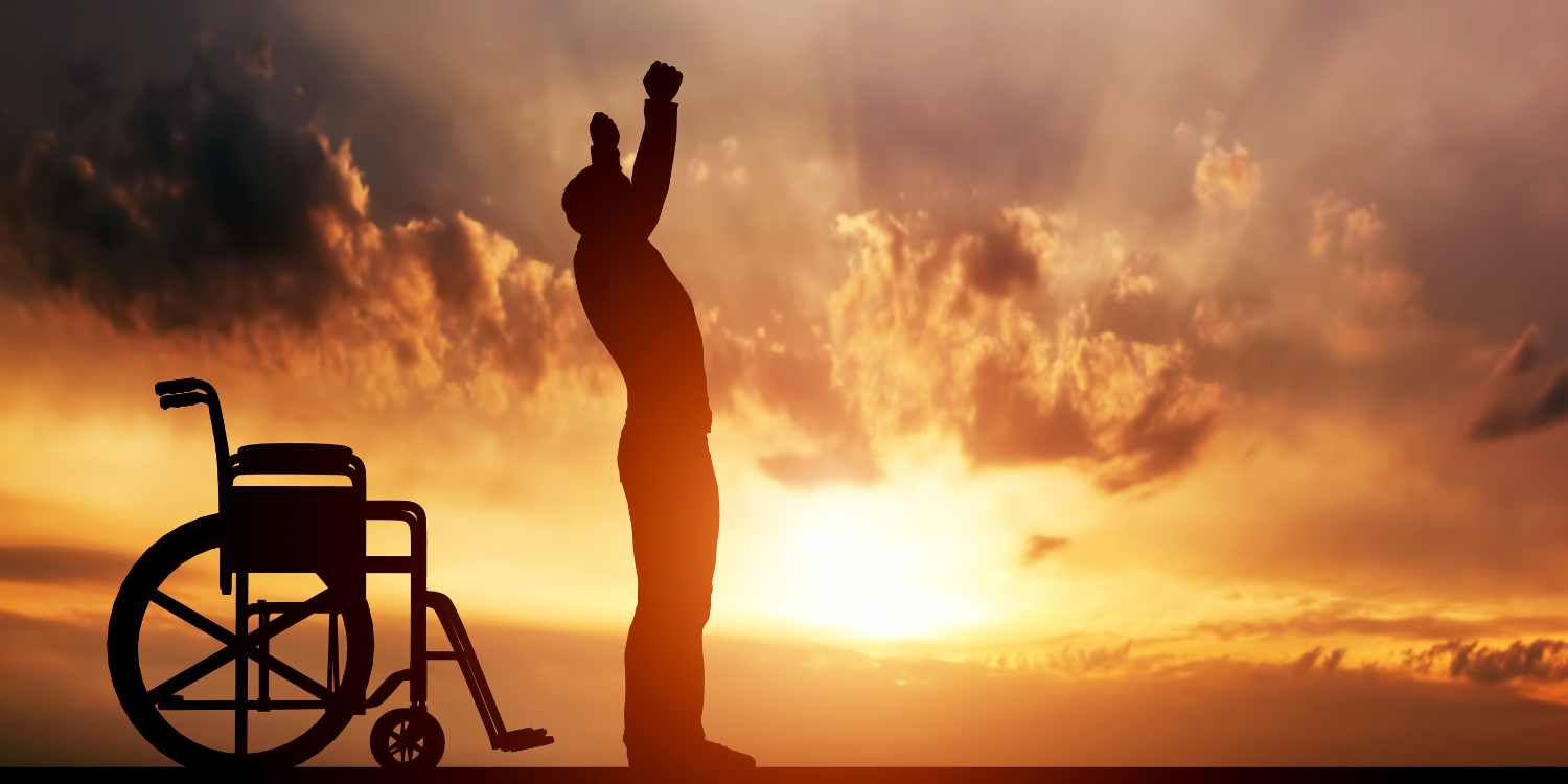Silhouette of a person standing beside a wheelchair at sunset.