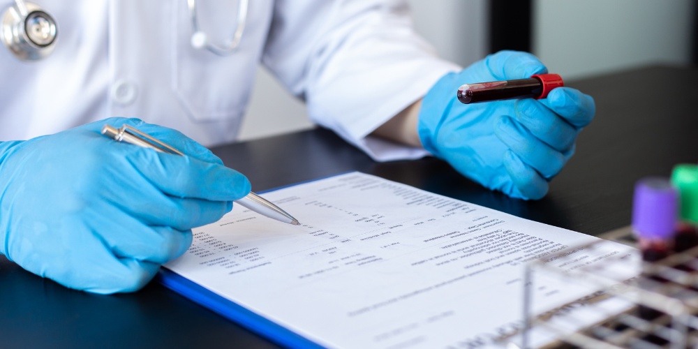 Person in gloves holding a blood sample and pointing at a document.