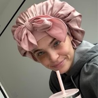 Person wearing a pink satin bonnet, holding a cup with a straw, and wearing a gray hoodie.