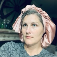 Person wearing a pink silk bonnet, with a neutral expression, in an indoor setting.