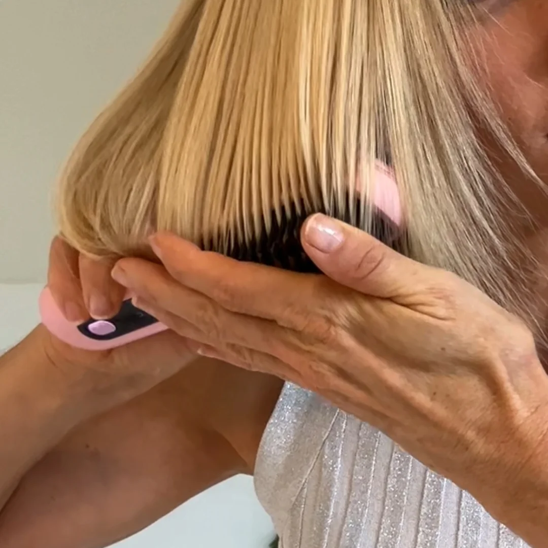 Person brushing blonde hair with a pink and black brush.