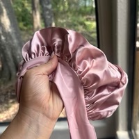 Hand holding a pink satin bonnet near a window with trees outside.