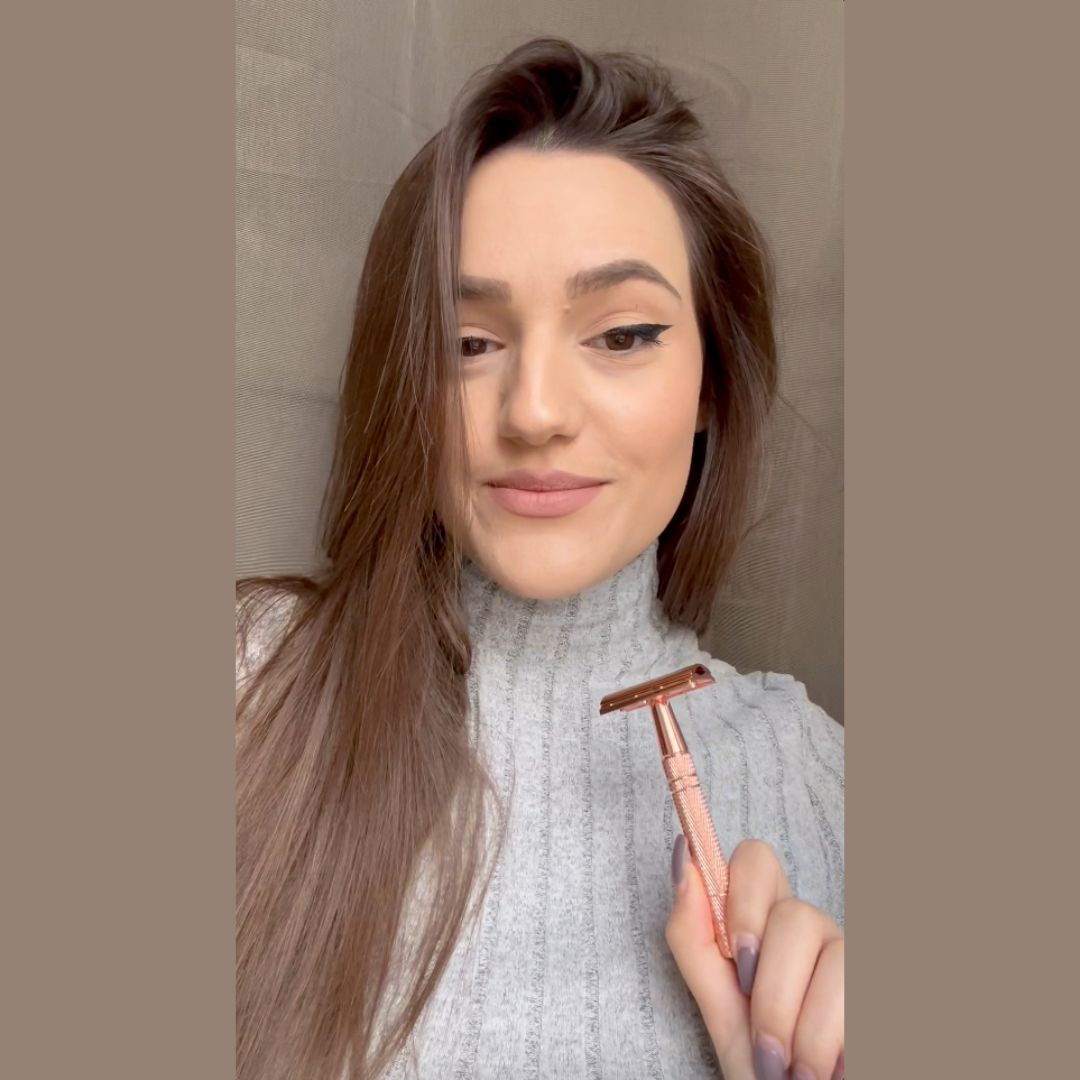 Person holding a rose gold safety razor, wearing a gray sweater.