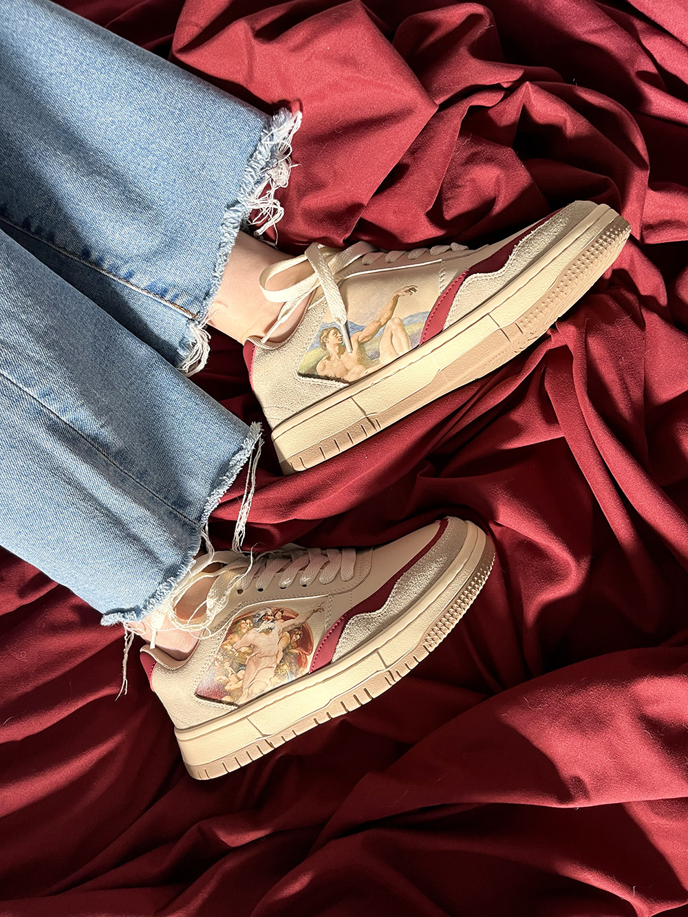 Denim jeans with artistic sneakers on a red fabric background.