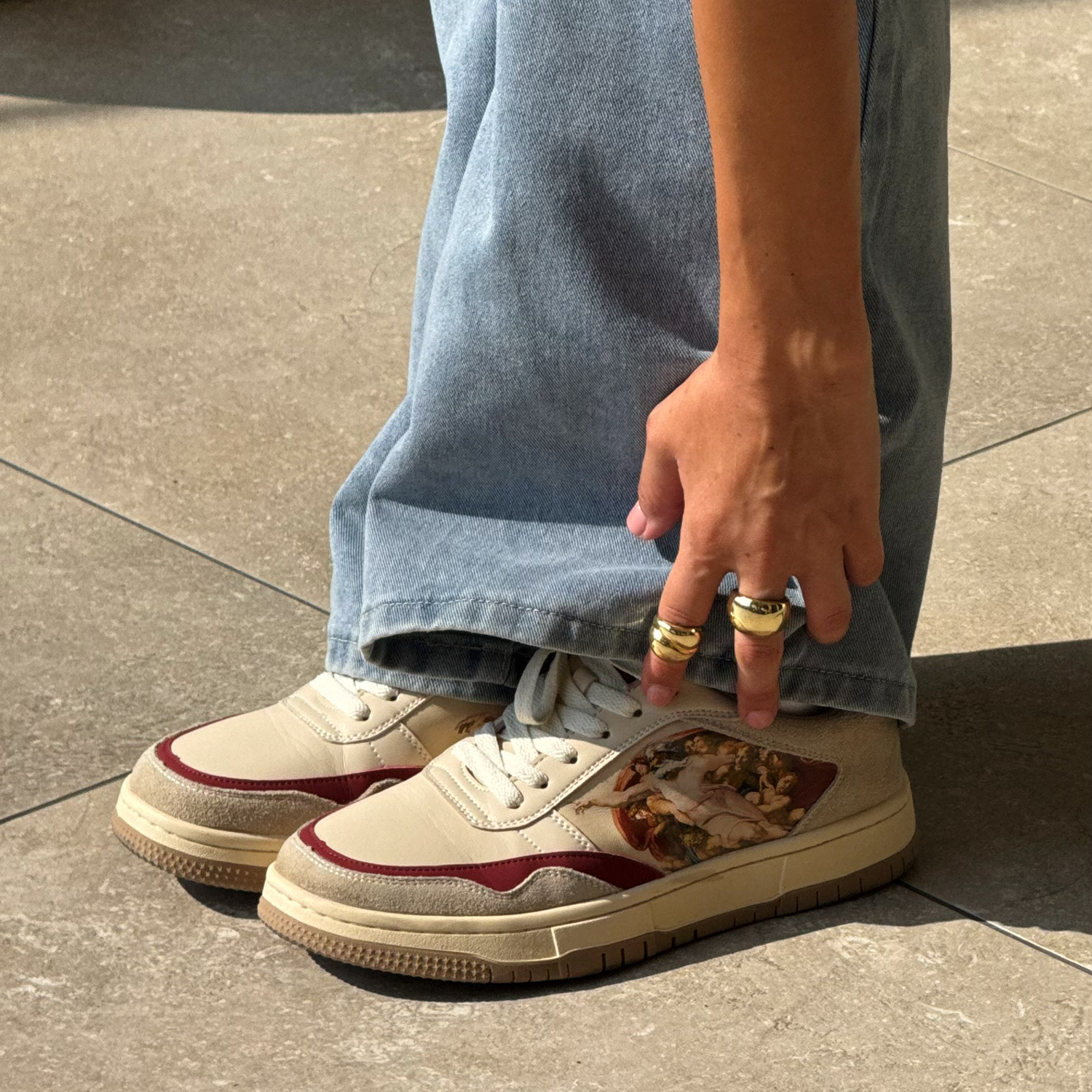 Person wearing sneakers with artwork design and loose jeans, touching the ground.