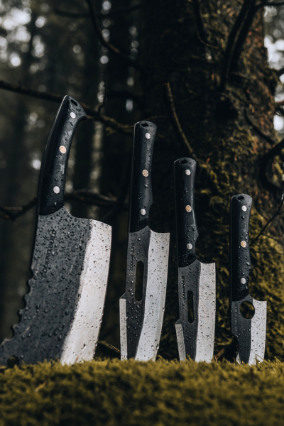 Four knives with black handles stuck in mossy ground in a forest.