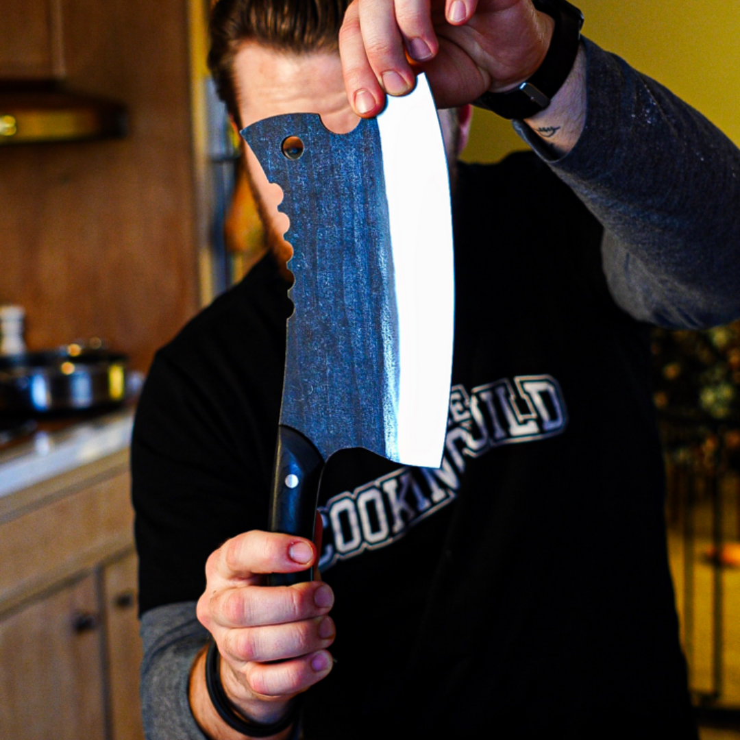 Person holding a large cleaver knife in a kitchen setting.