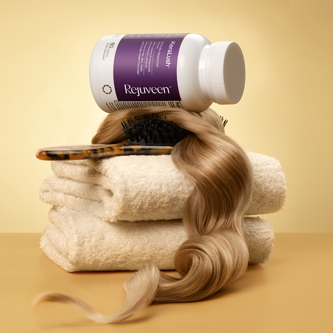 Hair supplement bottle on towels with brush and hair strand.