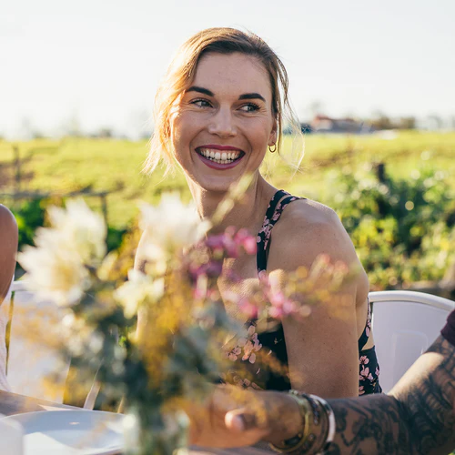 Smiling woman sitting outdoors with blurred flowers in the foreground.