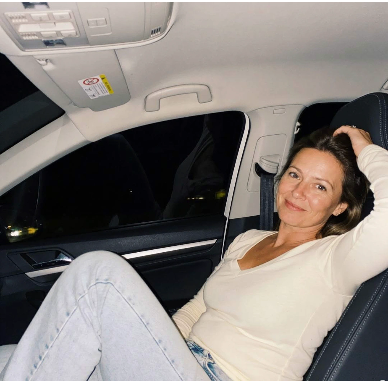 A woman smiles at the camera while sitting in the passenger seat of a car at night.