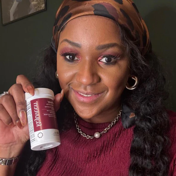 Person holding a bottle, smiling, wearing a headscarf and maroon top.