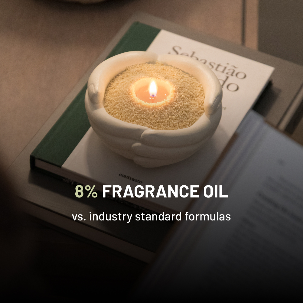 A lit candle with granular wax in a white hand-shaped holder sits on a stack of books.