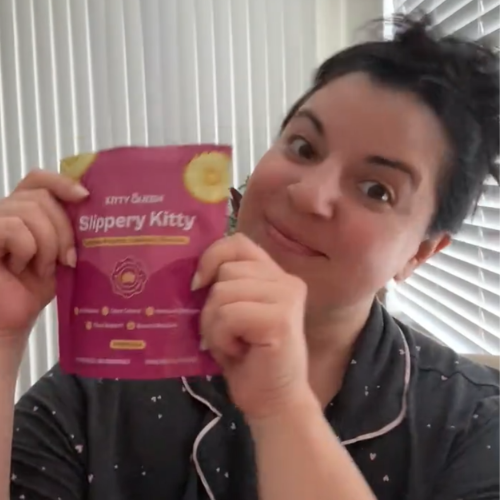 A woman with a playful expression holds up a pink pouch of a product called 'Slippery Kitty'.