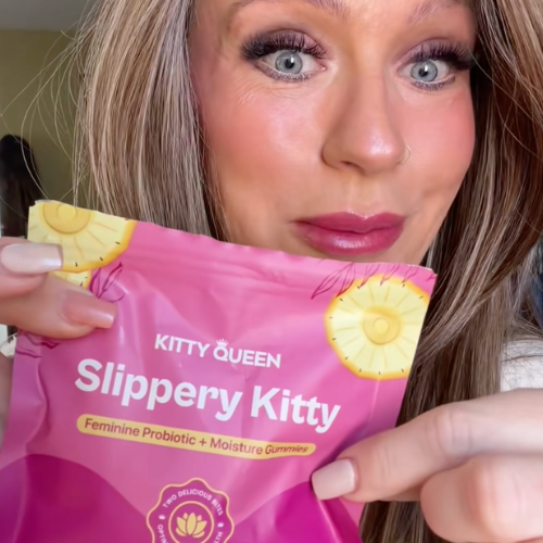 A woman holds up a pink package of Kitty Queen Slippery Kitty feminine probiotic gummies.