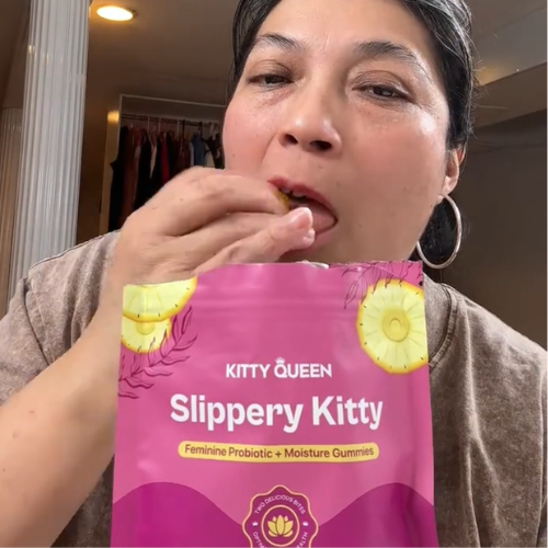 A person eats a gummy while holding a pink pouch of Kitty Queen Slippery Kitty gummies.