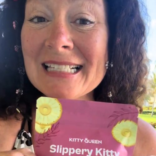 A smiling woman with dark curly hair holds a pink packet labeled 'Slippery Kitty'.
