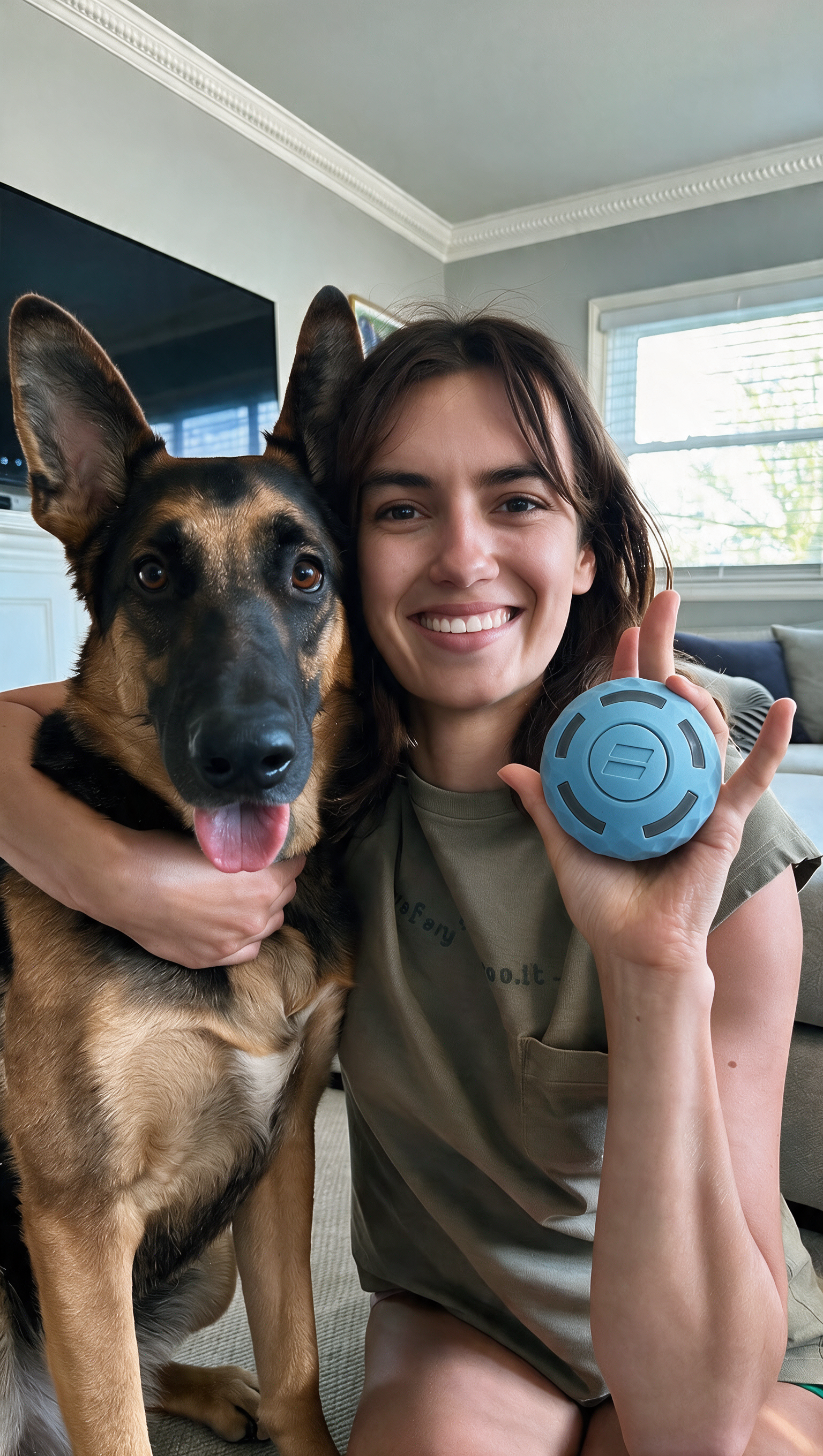 A smiling woman hugs a German Shepherd dog while holding a small, blue, circular object in her hand.