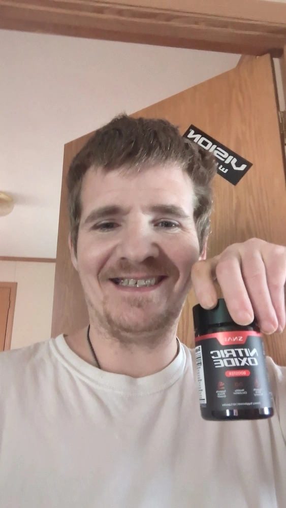 Person holding a bottle of nitric oxide booster in front of a wooden door.