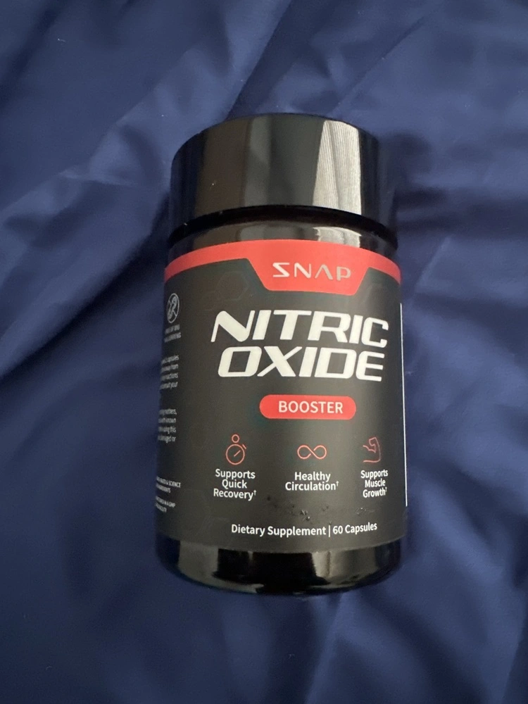 Black bottle labeled 'Nitric Oxide Booster' on a blue fabric background.