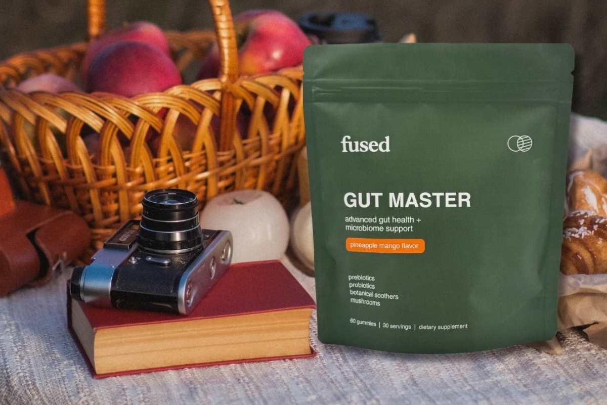 A pouch of Fused Gut Master supplement on a picnic blanket with a camera and a basket of apples.