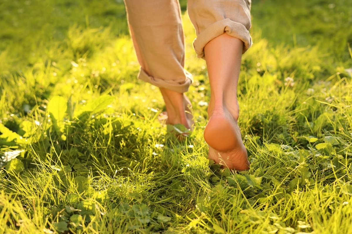A low-angle view of a person walking barefoot through lush green grass in the sunlight.
