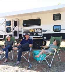 Three people sitting in chairs near an RV, smiling and wearing hats.