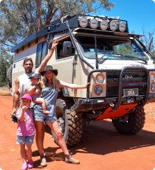 Family posing in front of a rugged off-road vehicle in a desert setting.
