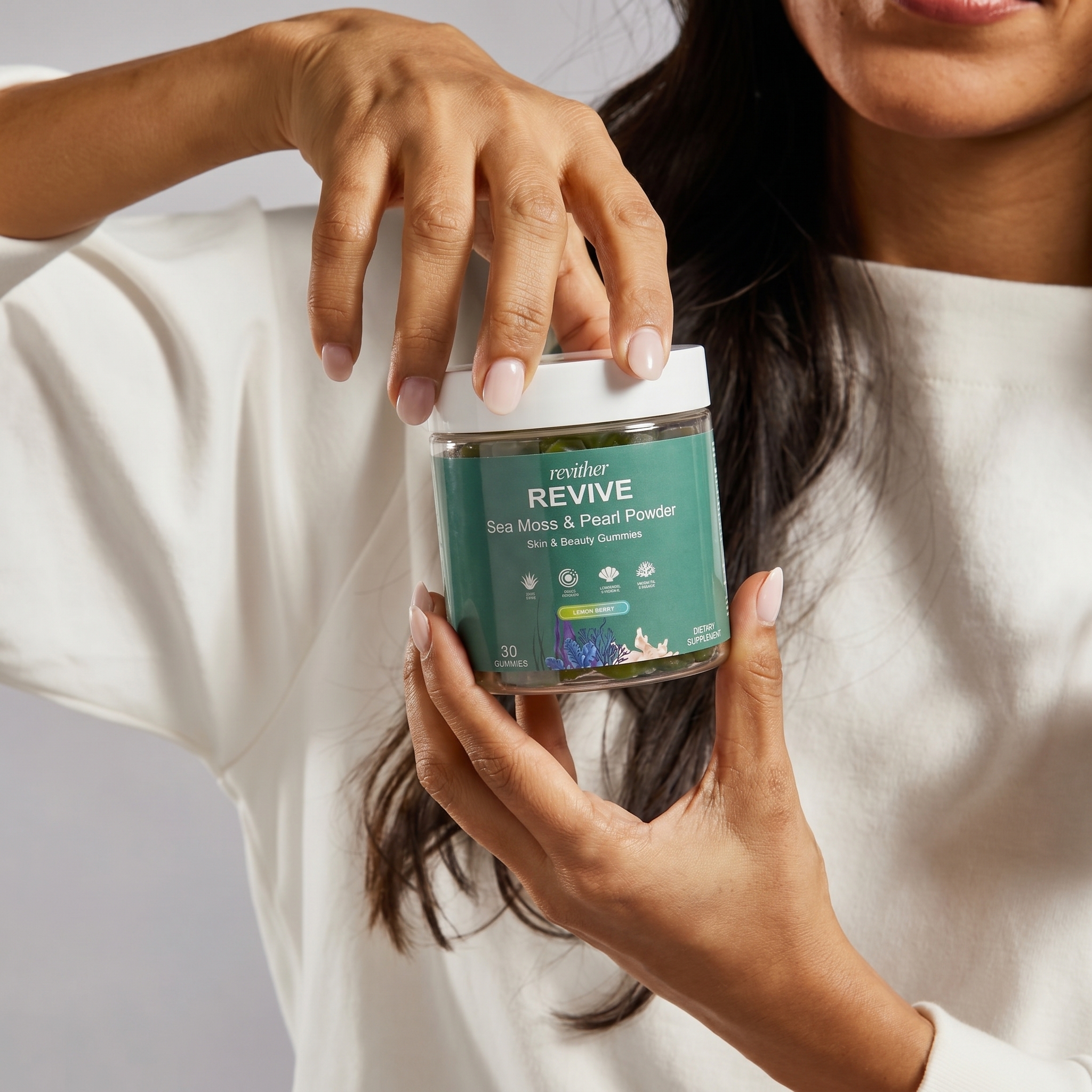 A person in a white shirt holds a jar of Revither Revive Sea Moss & Pearl Powder gummies.