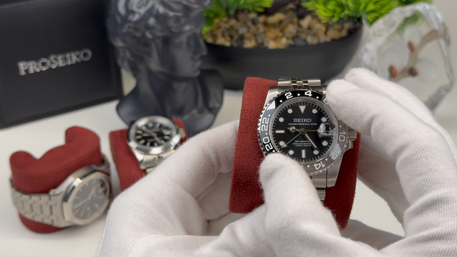 Gloved hands holding a Seiko watch with two other watches in the background.