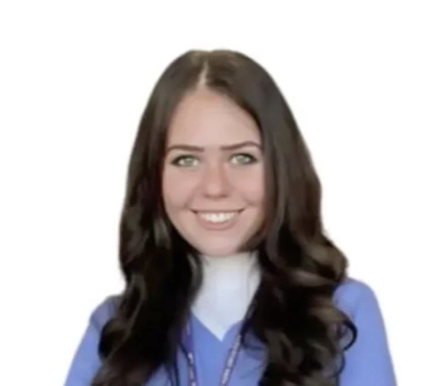 A headshot of a smiling young woman with long dark hair, wearing blue scrubs and a lanyard.