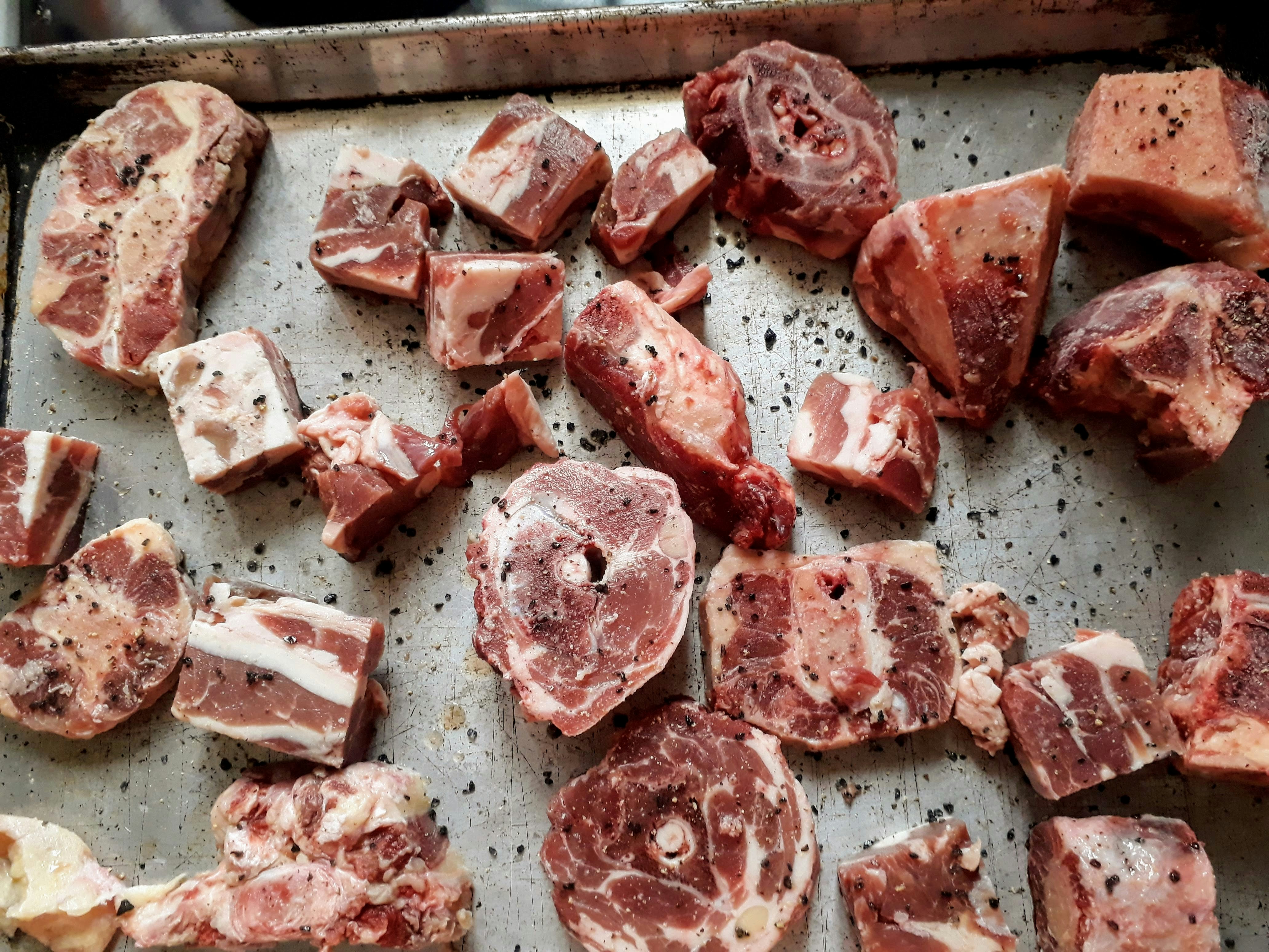 Raw bones on a roasting tray with spices all over.