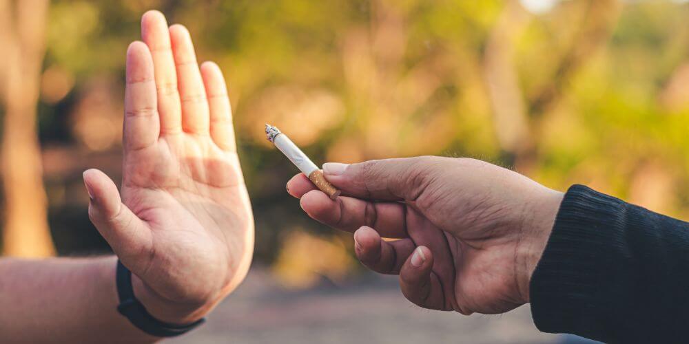 A hand rejecting a cigarette being offered outdoors.