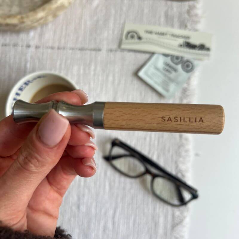 Hand holding a wooden and metal tool with 'SASILIA' engraved on the handle.