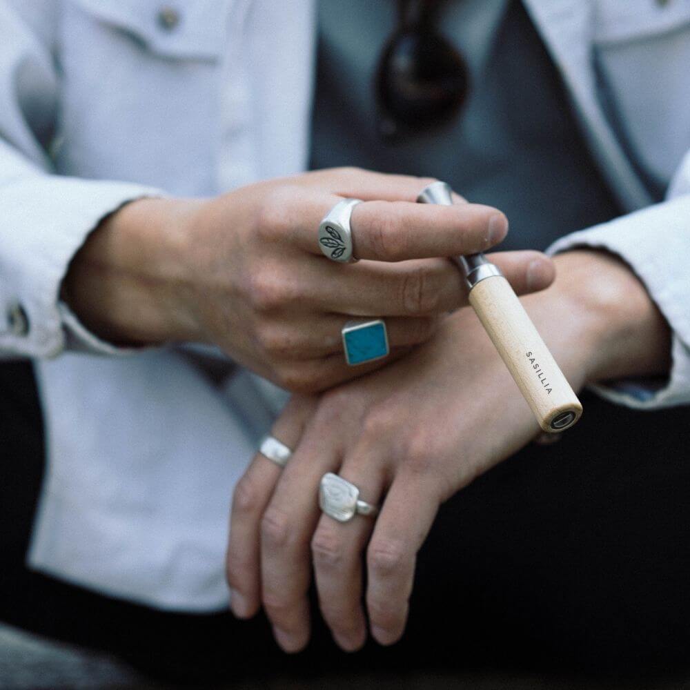 Person holding a vape pen with multiple rings on fingers.