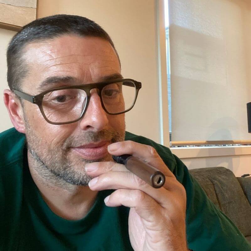 Man with glasses and a short haircut holding a cigar.