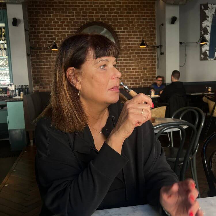 Woman sitting at a cafe table with a brick wall background.