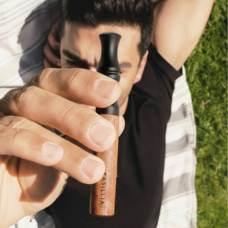 Person holding a wooden vape pen while lying on grass.