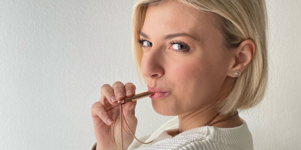 Person holding a whistle made of brass, positioned against a light background.