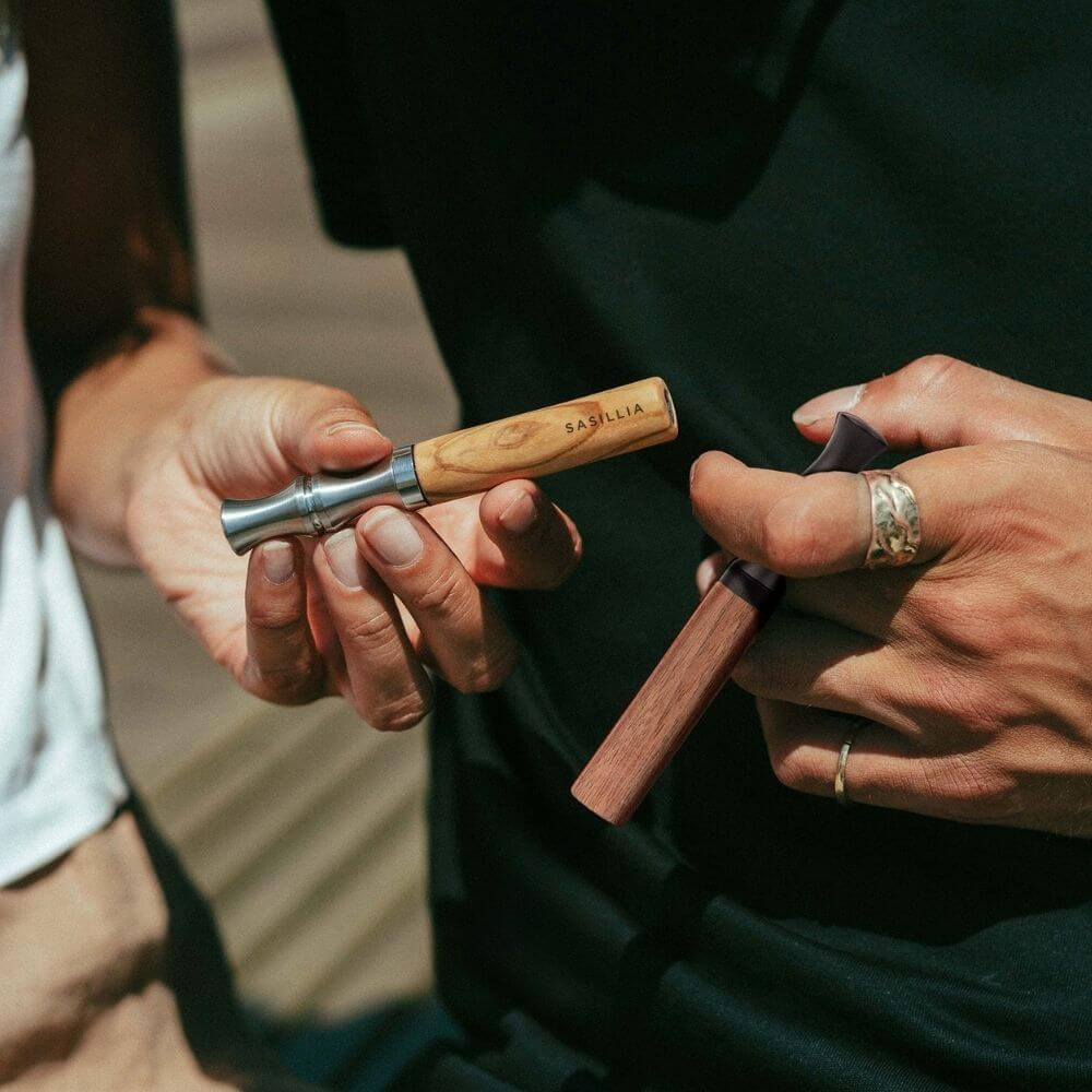 Two people holding wooden and metal smoking pipes.